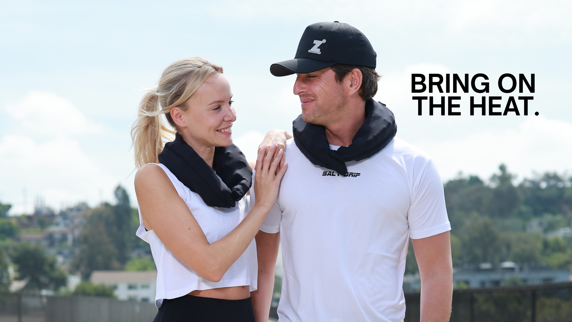 Two people wearing black HEROs with a scenic background and text 'BRING ON THE HEAT'.