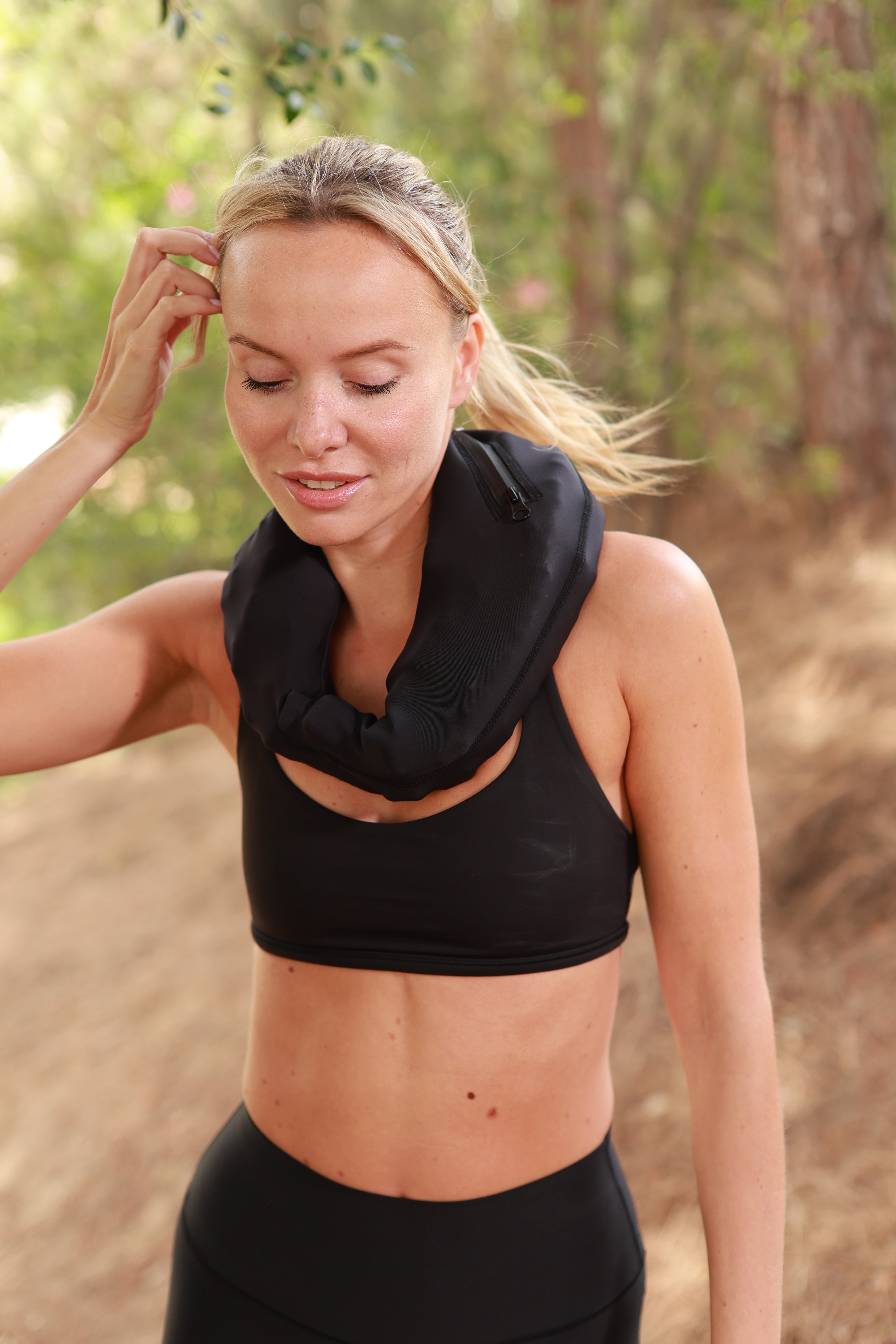 Woman in black athletic wear with a black neoprene pouch on her neck, while outdoors with blurred natural background.